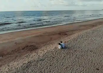 two people sits on sand beside seashore during daytime