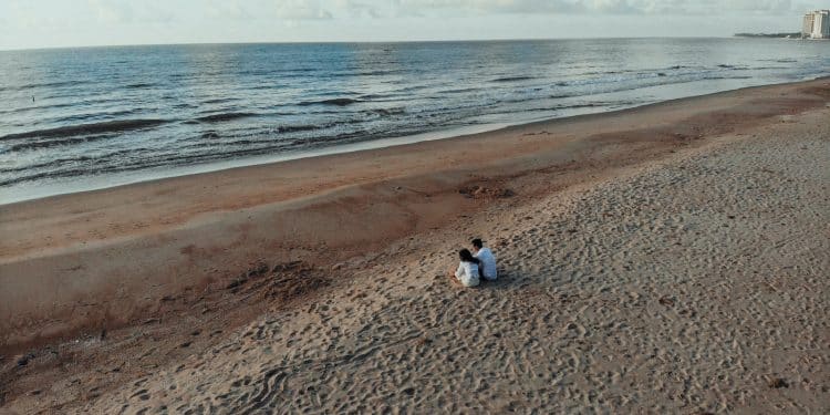 two people sits on sand beside seashore during daytime